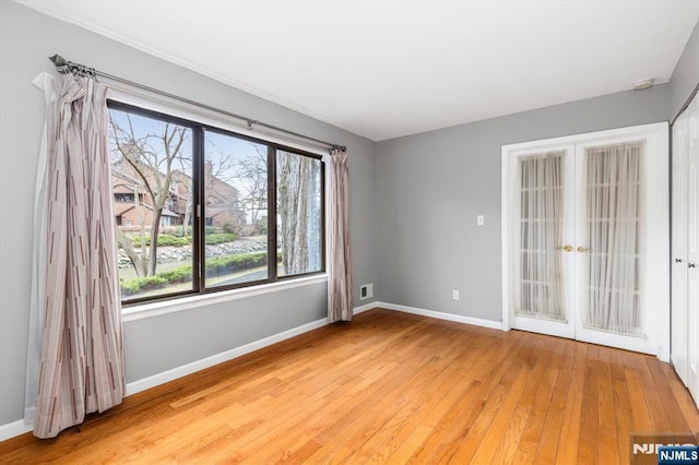 spare room featuring french doors, baseboards, and light wood-style flooring