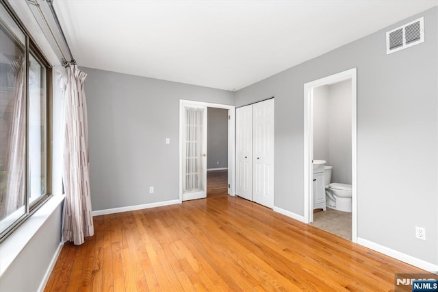 unfurnished bedroom featuring connected bathroom, light wood-style floors, visible vents, and baseboards