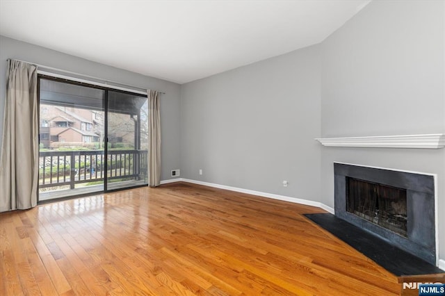 unfurnished living room with baseboards, a fireplace with flush hearth, and light wood finished floors