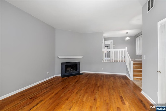 unfurnished living room featuring wood finished floors, visible vents, baseboards, a fireplace with flush hearth, and stairs