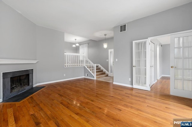 unfurnished living room featuring visible vents, baseboards, stairs, a fireplace, and wood finished floors