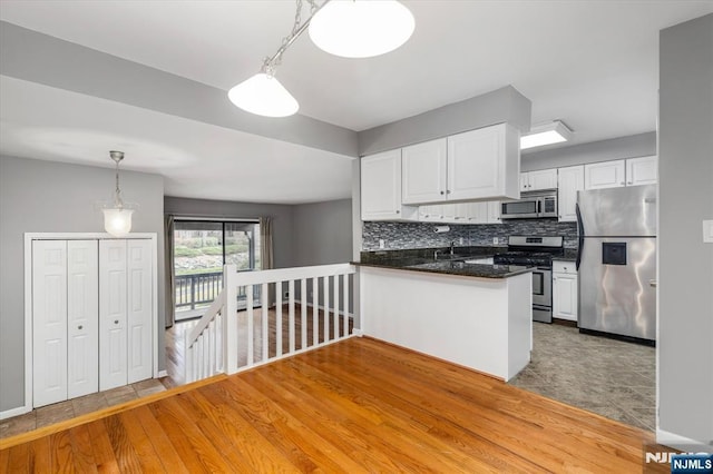 kitchen with backsplash, dark countertops, white cabinetry, stainless steel appliances, and a peninsula