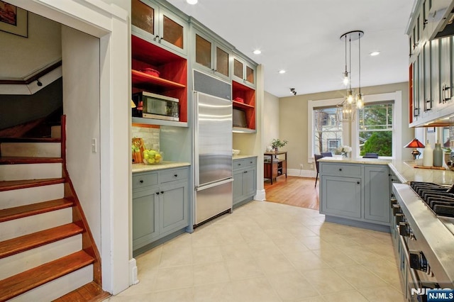 kitchen with high end appliances, light countertops, gray cabinetry, pendant lighting, and backsplash