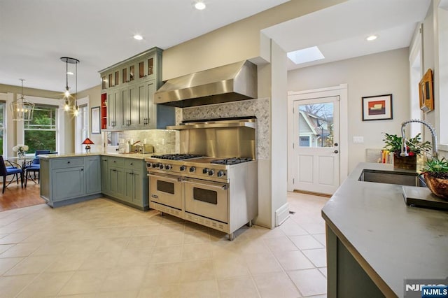 kitchen featuring decorative backsplash, a sink, double oven range, a peninsula, and wall chimney exhaust hood