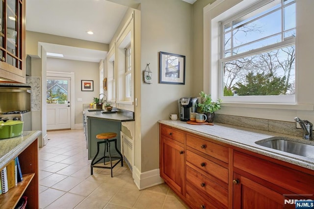 kitchen featuring baseboards, glass insert cabinets, a sink, and light tile patterned flooring