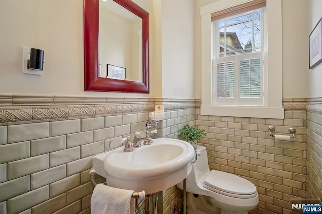 bathroom featuring wainscoting, a sink, tile walls, and toilet