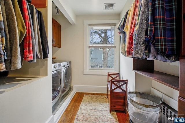 laundry area featuring cabinet space, visible vents, radiator heating unit, light wood-style flooring, and washing machine and dryer