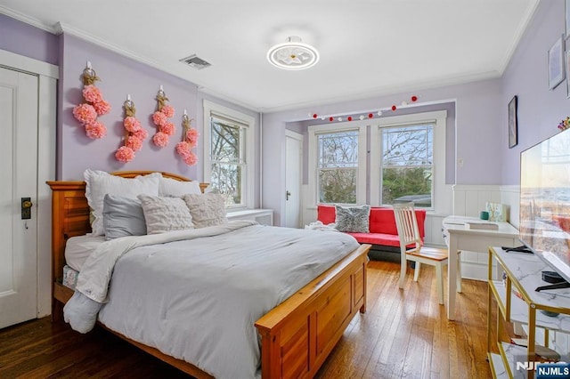 bedroom with hardwood / wood-style floors, multiple windows, wainscoting, and visible vents