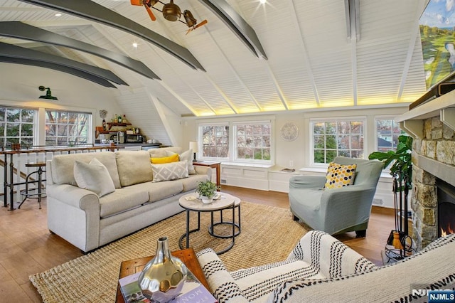 living room with vaulted ceiling with beams, wood finished floors, and a stone fireplace