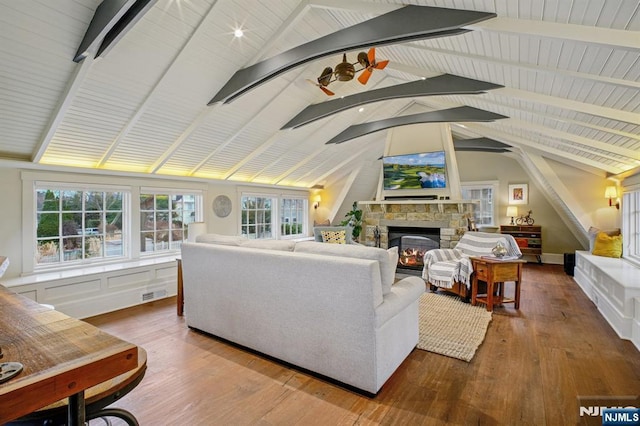 living room featuring lofted ceiling with beams, ceiling fan, hardwood / wood-style floors, and a stone fireplace