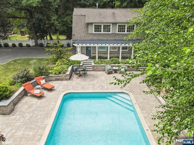 back of property featuring a fenced in pool, a shingled roof, a patio area, fence, and stone siding