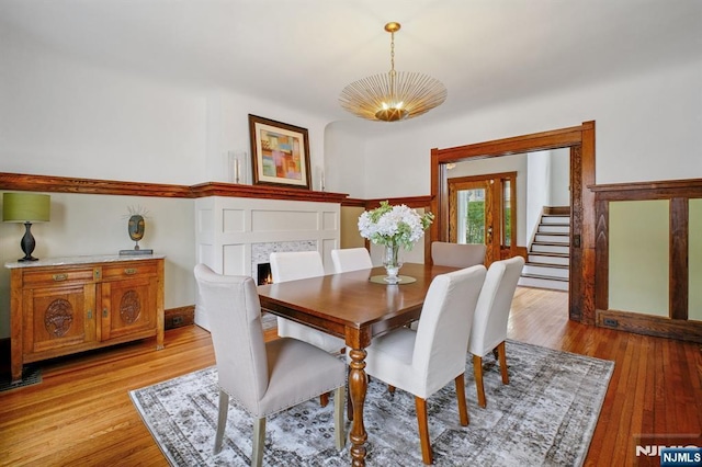 dining area with light wood-style floors, a notable chandelier, a lit fireplace, and stairs