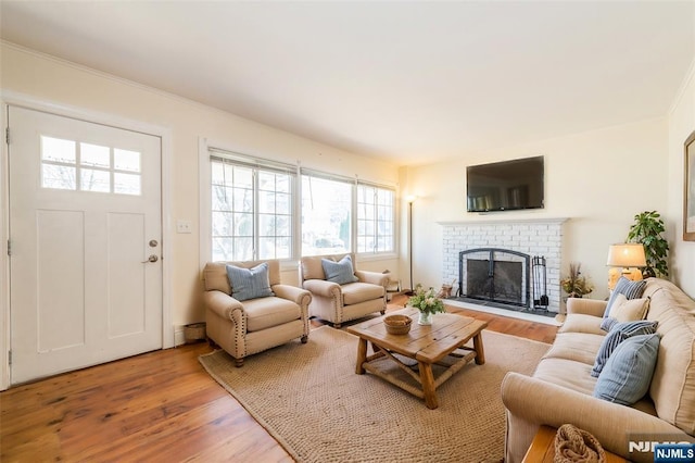 living room with ornamental molding, a brick fireplace, light wood-style floors, and a baseboard radiator