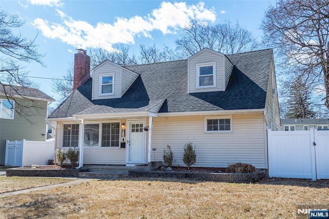 cape cod home with roof with shingles, a front lawn, and fence