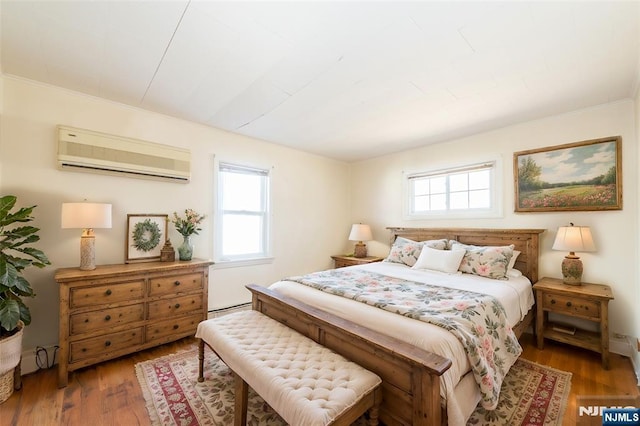 bedroom featuring a wall mounted air conditioner, a baseboard heating unit, and wood finished floors