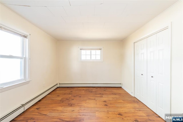 unfurnished bedroom with a closet, baseboard heating, light wood-style flooring, and crown molding