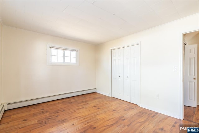 unfurnished bedroom featuring baseboards, ornamental molding, baseboard heating, wood finished floors, and a closet