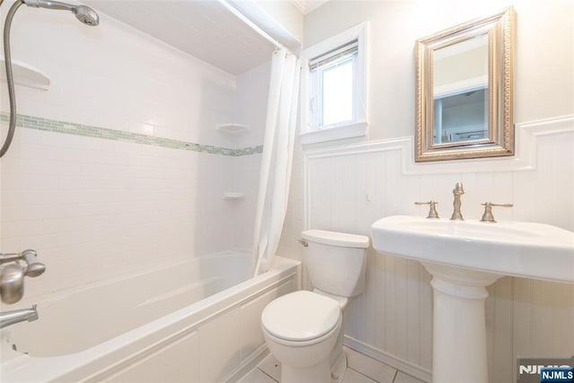 full bathroom featuring tile patterned flooring, a wainscoted wall, toilet, shower / bath combo with shower curtain, and a sink