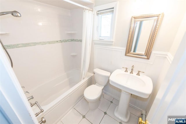 bathroom featuring tile patterned floors, toilet, shower / bathtub combination with curtain, and a wainscoted wall