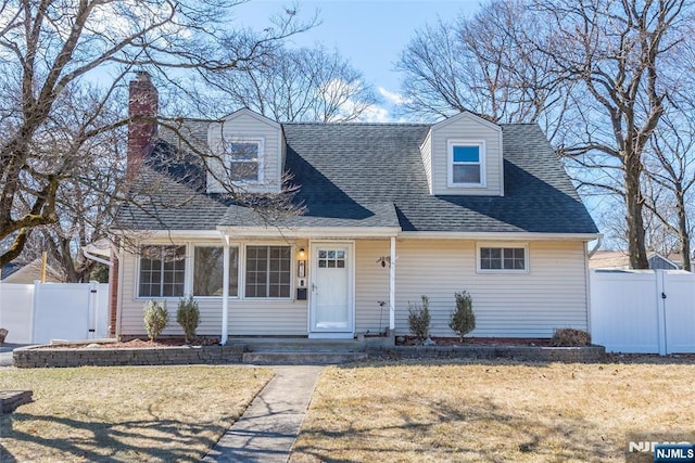 cape cod home with a front lawn, a gate, fence, roof with shingles, and a chimney