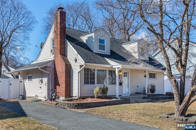 cape cod-style house with a gate, fence, roof with shingles, a chimney, and a front lawn