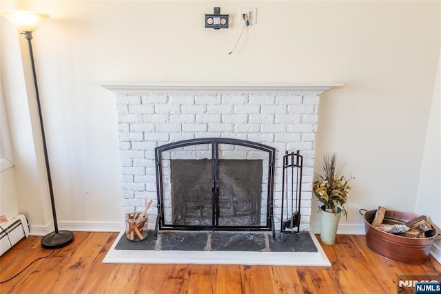 room details featuring a fireplace, a baseboard heating unit, baseboards, and wood finished floors