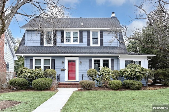 view of front of house with a shingled roof, a chimney, and a front lawn