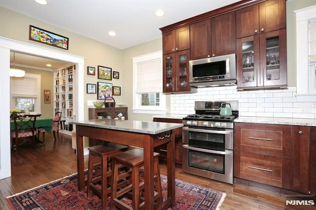 kitchen with stainless steel appliances, glass insert cabinets, dark wood finished floors, and decorative backsplash