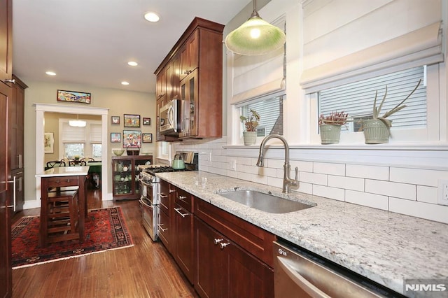 kitchen with decorative backsplash, light stone counters, dark wood-style flooring, stainless steel appliances, and a sink