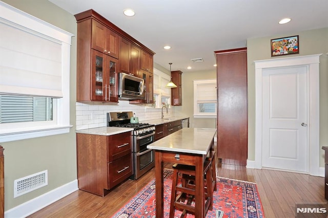 kitchen featuring stainless steel appliances, a sink, wood finished floors, visible vents, and light countertops