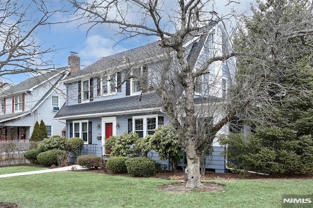 view of front of property with a shingled roof, a front yard, and a chimney