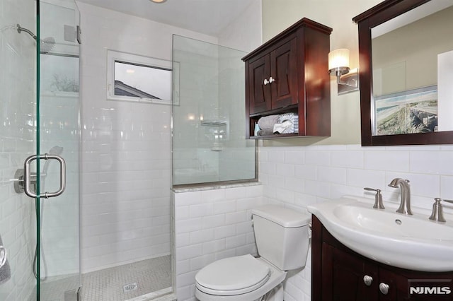 bathroom featuring tile walls, a shower stall, toilet, and vanity