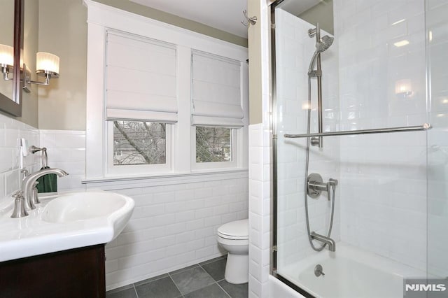 bathroom with shower / bath combination with glass door, tile walls, toilet, vanity, and tile patterned floors