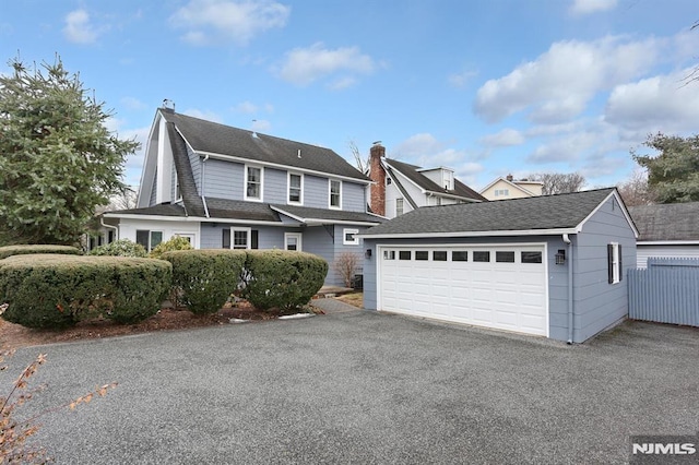 view of front of house with a garage, an outdoor structure, a chimney, and a shingled roof