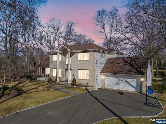 view of front of home featuring a garage, brick siding, a yard, and aphalt driveway