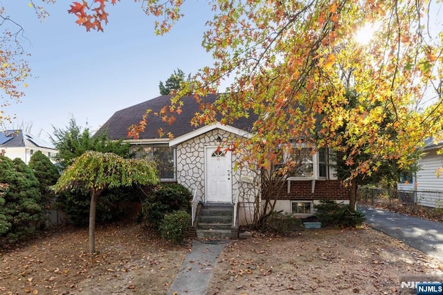 view of front of house featuring entry steps, a shingled roof, fence, stone siding, and driveway