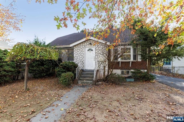 bungalow-style home with stone siding, brick siding, and fence