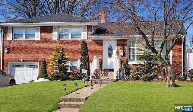 split level home with an attached garage, brick siding, a shingled roof, a front lawn, and a chimney