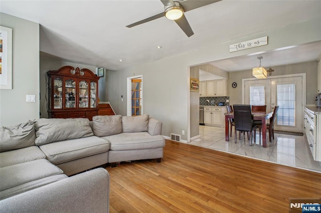 living area featuring light wood finished floors, baseboards, visible vents, and ceiling fan