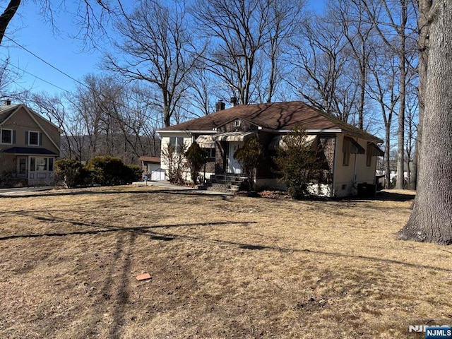 view of front facade featuring brick siding, crawl space, and a chimney