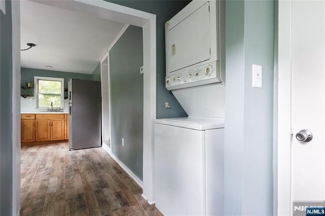 laundry room with stacked washer and dryer, wood finished floors, a sink, and laundry area