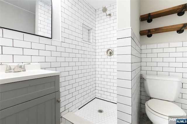 full bathroom featuring a tile shower, tile walls, toilet, and vanity