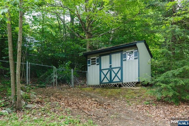 view of shed with a gate, fence, and a view of trees