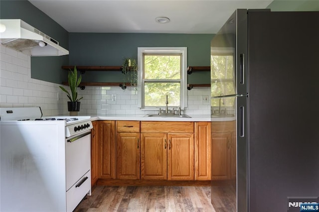 kitchen featuring open shelves, freestanding refrigerator, a sink, under cabinet range hood, and white gas range oven