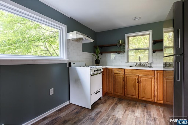 kitchen with white range with gas cooktop, freestanding refrigerator, under cabinet range hood, open shelves, and a sink