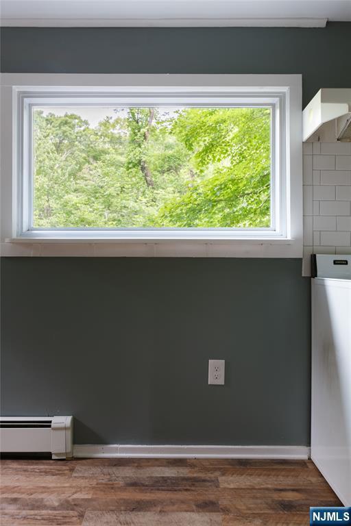 interior details featuring tasteful backsplash, baseboard heating, wood finished floors, and washer / dryer