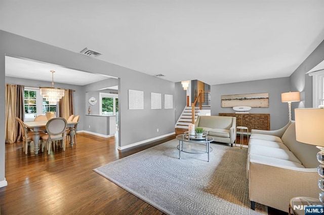 living area featuring visible vents, baseboards, stairway, wood finished floors, and a notable chandelier