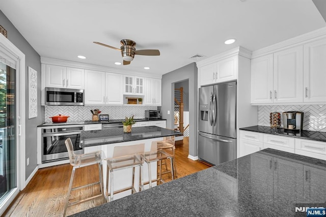 kitchen featuring white cabinets, dark stone counters, wood finished floors, stainless steel appliances, and a kitchen bar