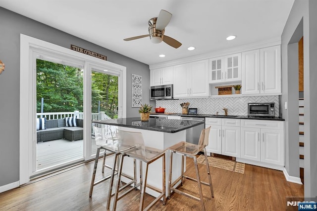 kitchen with white cabinets, decorative backsplash, light wood-style flooring, appliances with stainless steel finishes, and a breakfast bar