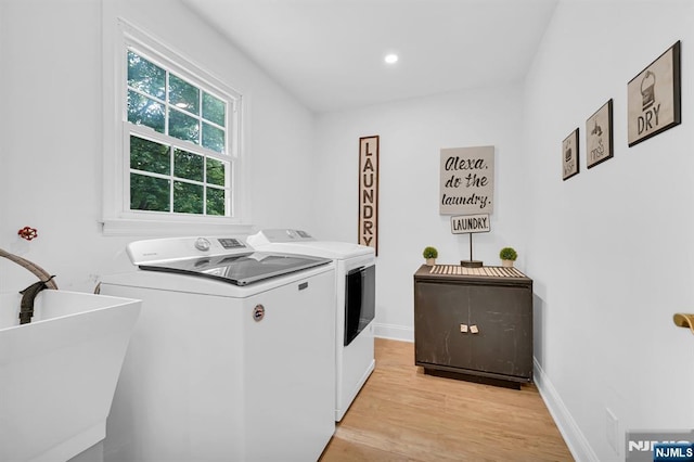 laundry area with laundry area, light wood finished floors, baseboards, washing machine and dryer, and a sink